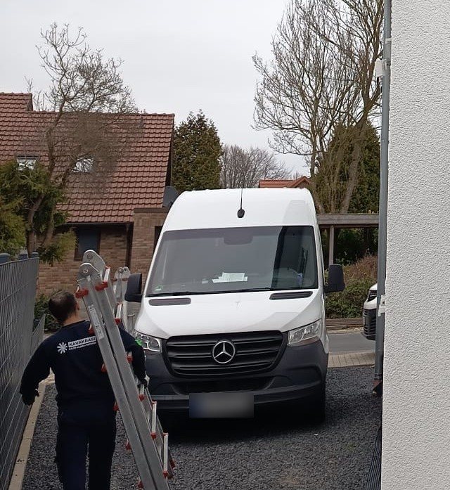 Kavakbasi-Monteur mit Leiter auf dem Weg zum Einsatz, Firmenwagen im Hintergrund